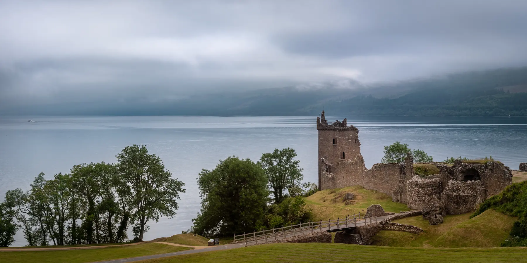 Urquhart Castle overlooking Loch Ness beneath cloud-covered mountains
