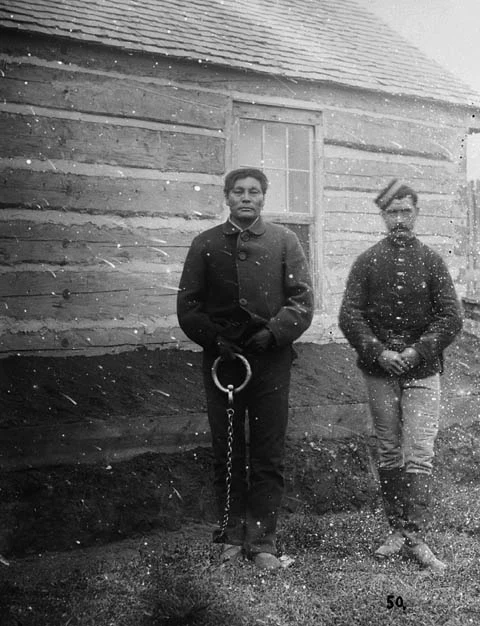 Swift Runner standing in shackles at Fort Saskatchewan after his arrest in 1879